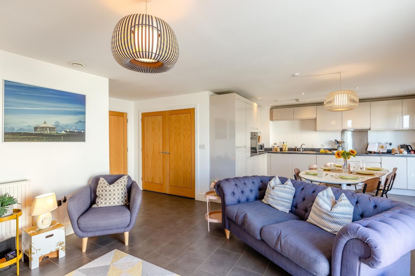 A modern living room with a sofa, a dining table, and a kitchen in the background.