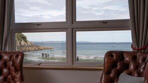Une pièce avec deux fauteuils en cuir placés face à une fenêtre donnant sur une côte rocheuse et la mer.