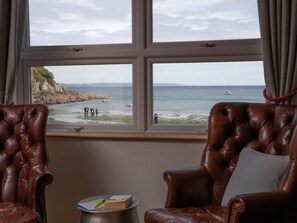 Ein Zimmer mit zwei Ledersesseln, die zu einem Fenster mit Blick auf eine felsige Küstenlinie und das Meer ausgerichtet sind.