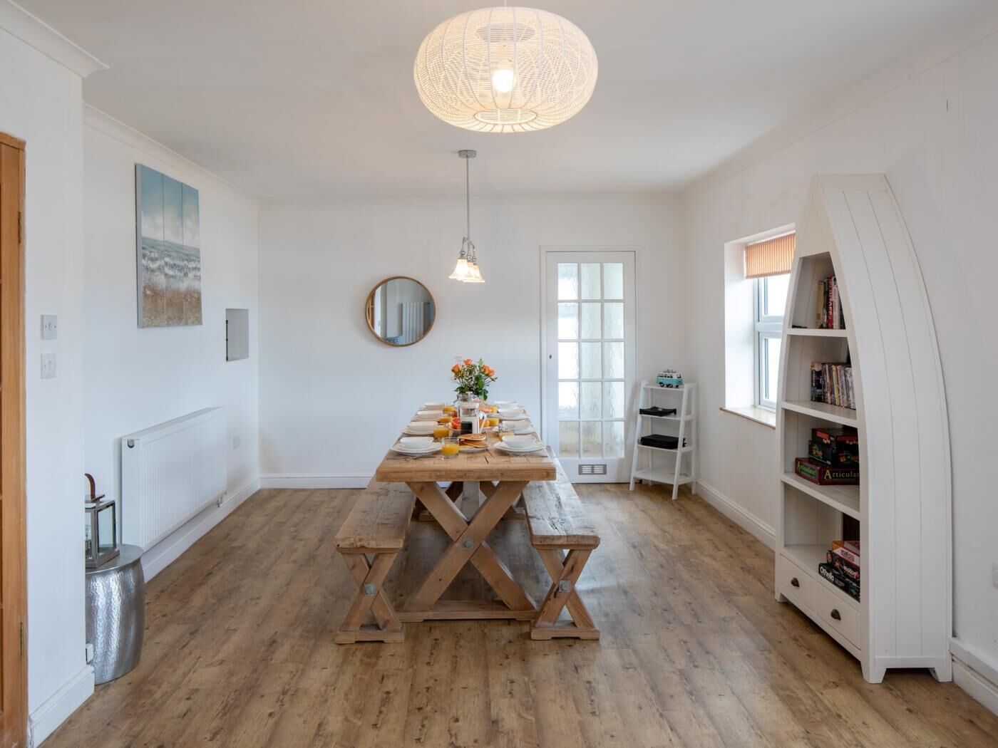 Un coin repas avec une table et des bancs en bois, un luminaire suspendu, une bibliothèque et un radiateur.