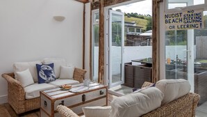 Une pièce chaleureuse, meublée de meubles en osier, avec un canapé, une table basse et une porte-fenêtre coulissante donnant sur un espace extérieur.