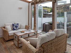 Ein gemütliches Zimmer mit Korbmöbeln, einer Couch, einem Couchtisch und einer Schiebetür zu einem Außenbereich.