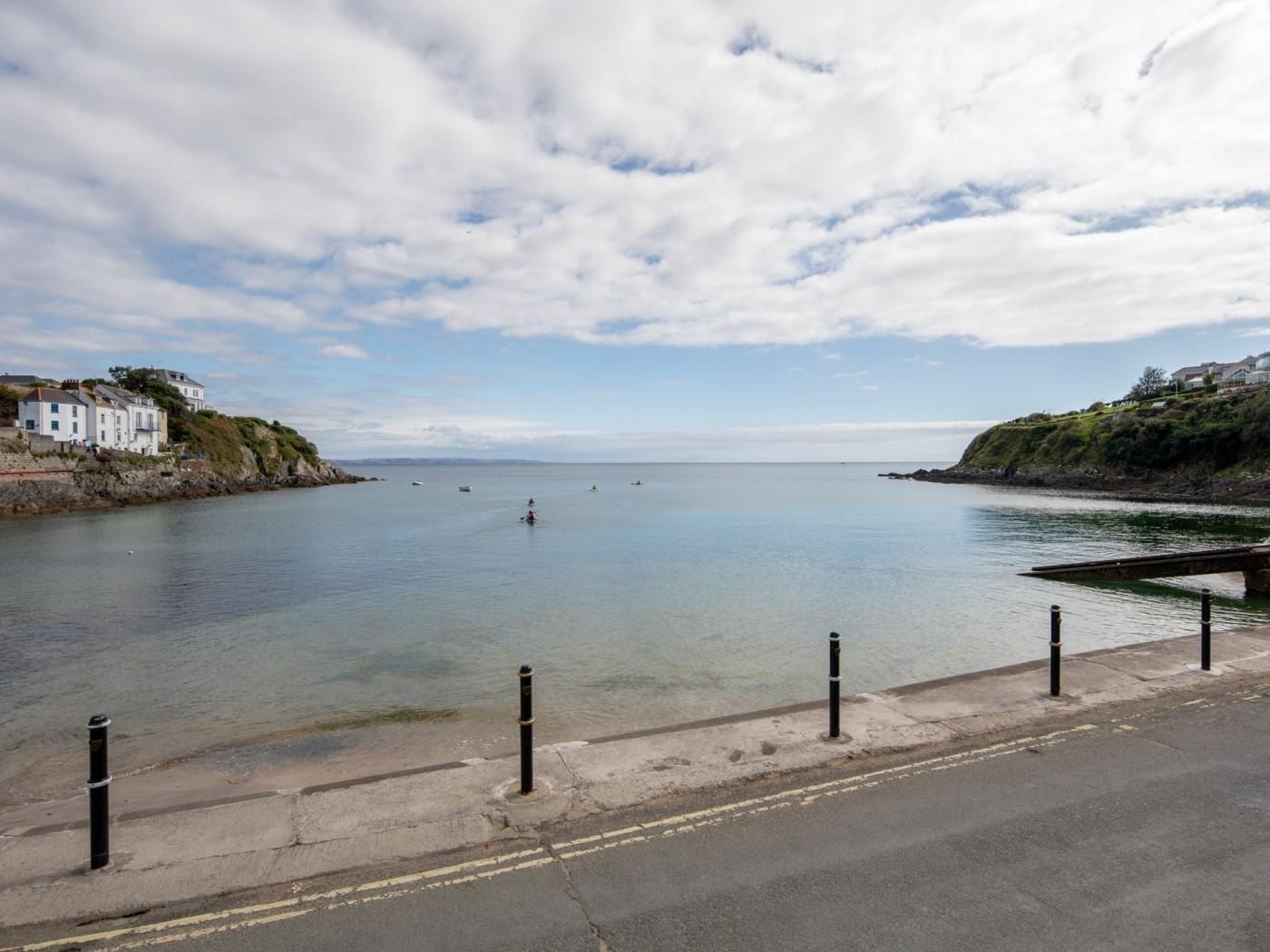 A coastal road with a clear view of the sea, a bridge, and buildings on the shore.