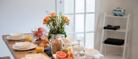Una tavola imbandita per la colazione con piatti, ciotole, bicchieri e una coppetta di frutta.