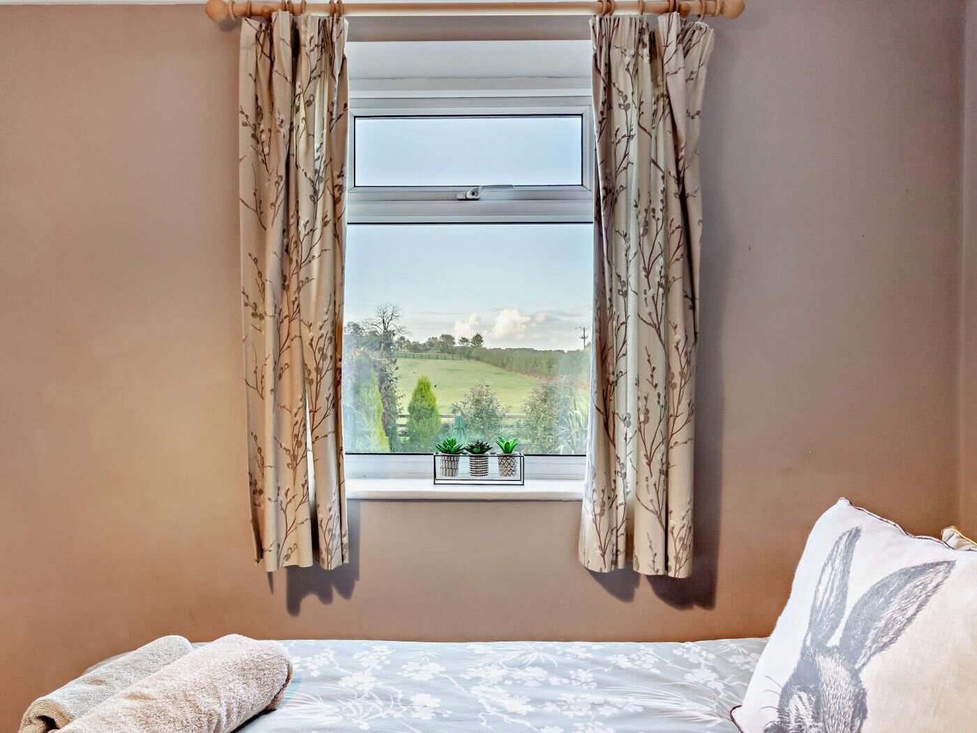 Ein Schlafzimmer mit einem Bett, einem Fenster mit Vorhängen und Blick auf eine grüne Landschaft.