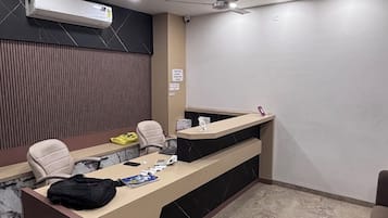 Un mostrador de recepción con una computadora, un teléfono y un bolso encima. Hay una silla y una lámpara de escritorio.