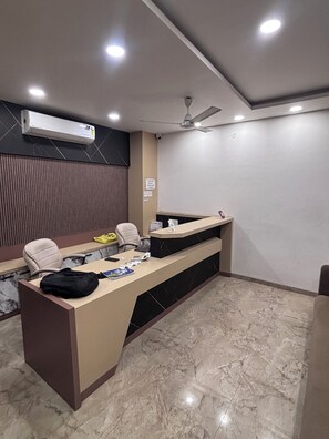 A reception desk with a computer, a telephone, and a bag on it. There is a chair and a desk lamp.