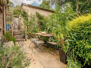 A patio with a table and chairs, surrounded by lush greenery and a wooden fence. - 3 Bed in Abergavenny (oc-48309) (Forest Coal Pit)