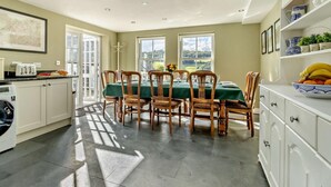 Un coin repas avec une table dressée pour six personnes, entourée de chaises, et offrant une vue sur la verdure à l’extérieur.