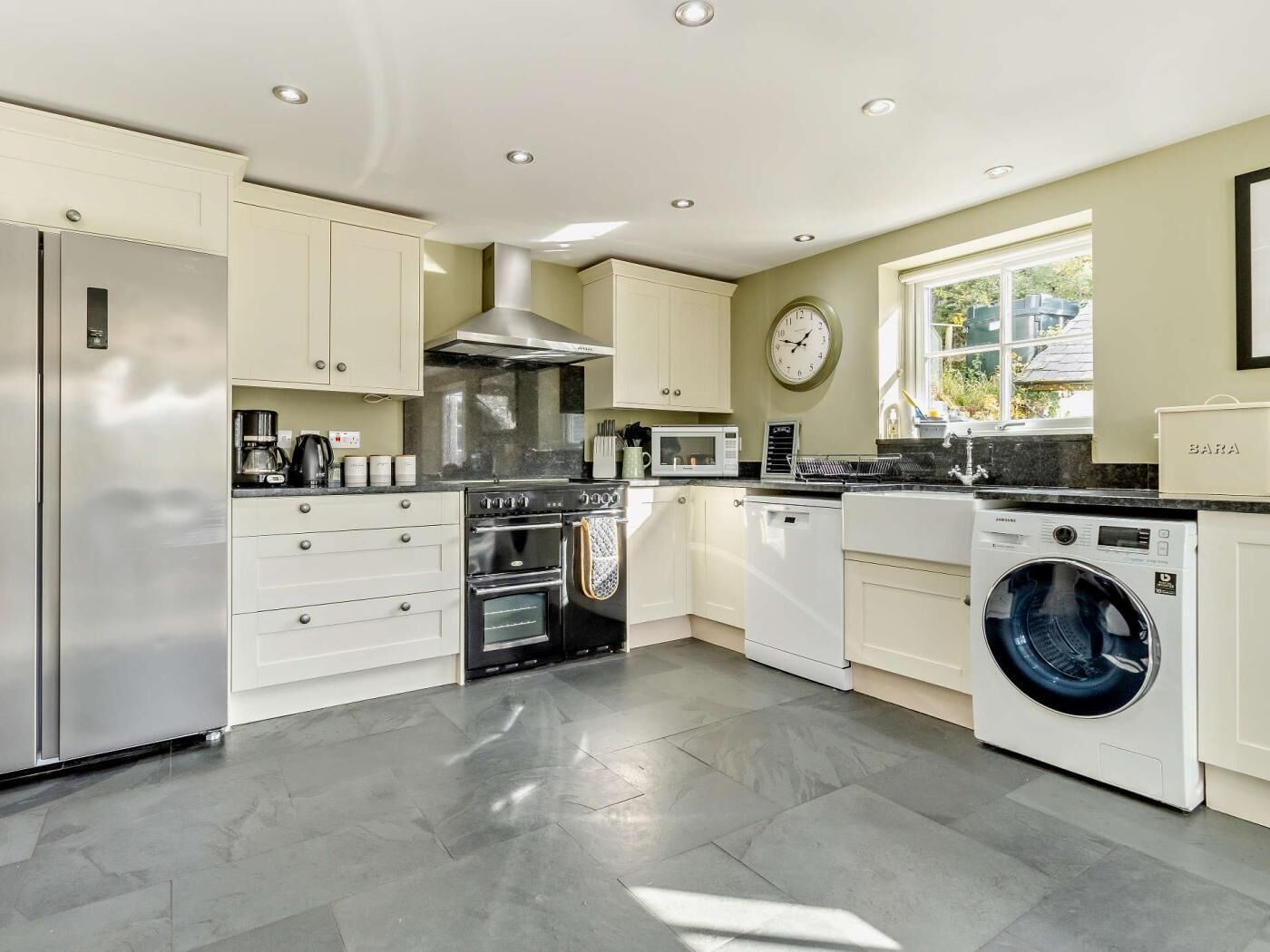A modern kitchen with a stainless steel refrigerator, double ovens, a microwave, a washing machine, and a clock on the wall.