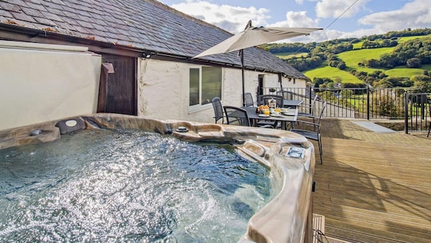 Un espace avec un jacuzzi, une table et des chaises, un patio couvert et une vue sur des collines verdoyantes.