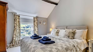 Une chambre avec un grand lit, une fenêtre avec des rideaux, une table de chevet avec une lampe, et une vue sur l’extérieur.