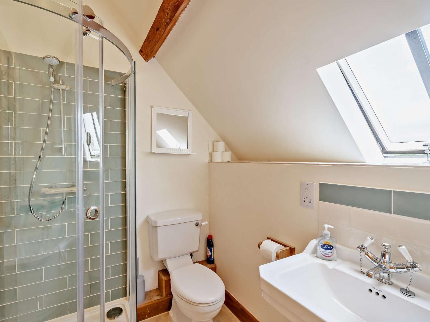 Een badkamer met een douchecabine van glas, toilet, wastafel met spiegel en dakraam.
