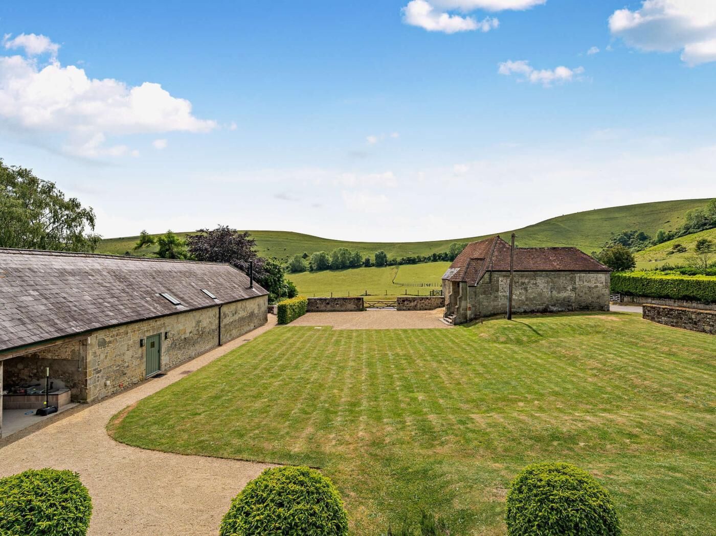 A rural property with a large lawn, stone buildings, and a clear sky.
