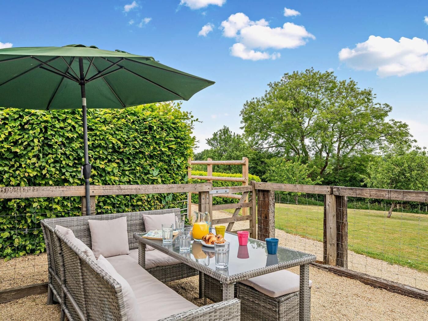 An outdoor seating area with wicker furniture, a glass table, and a green umbrella.