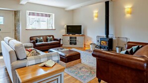 A living room with a sofa, armchair, ottoman, TV, fireplace, and a window with a view. - 3 Bed in Shaftesbury (oc-48804) (East Melbury)