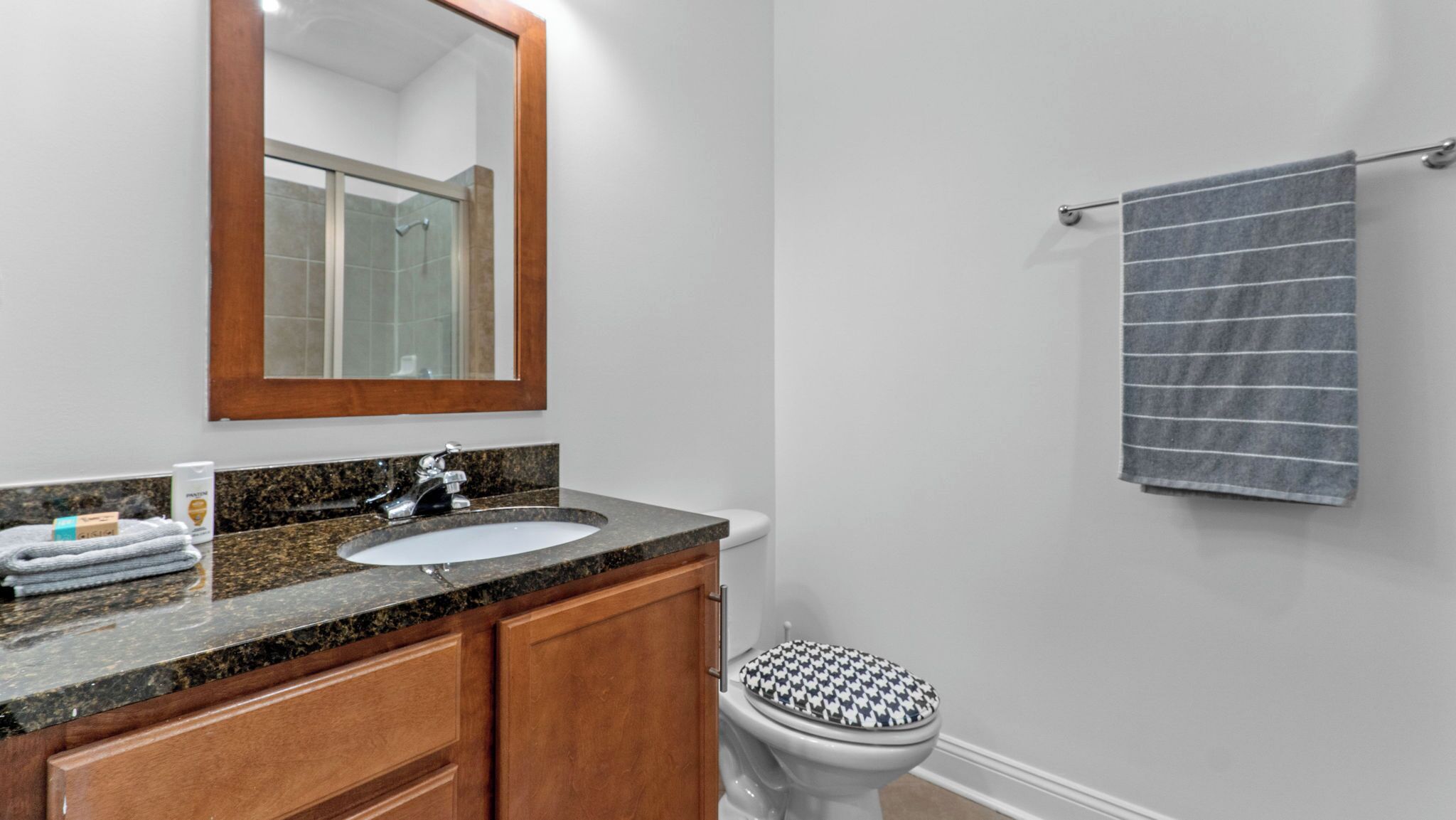 Baño con lavamanos de encimera de granito, muebles de madera, inodoro blanco y toallero con una toalla a rayas.