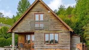 Een rustieke houten chalet met balkon, een eethoek met tafel en stoelen, en een klein terras.