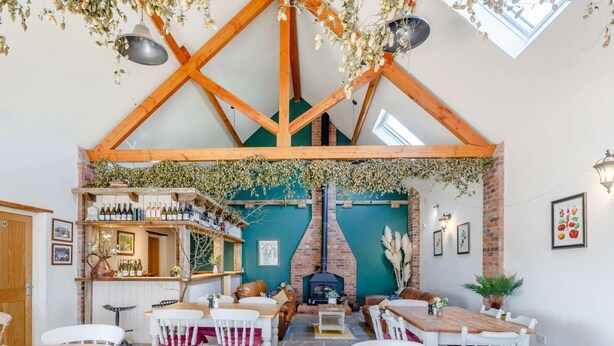 Een rustiek interieur met zichtbare houten balken, een open haard van baksteen en een bar met wijnflessen.