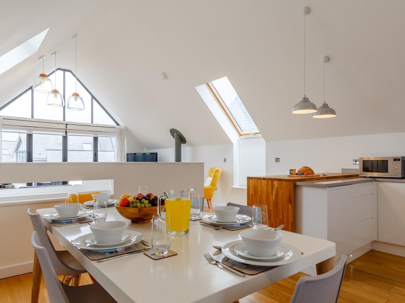 Una cocina moderna con comedor, que incluye una mesa larga dispuesta para dos personas, un frutero y un vaso de jugo.