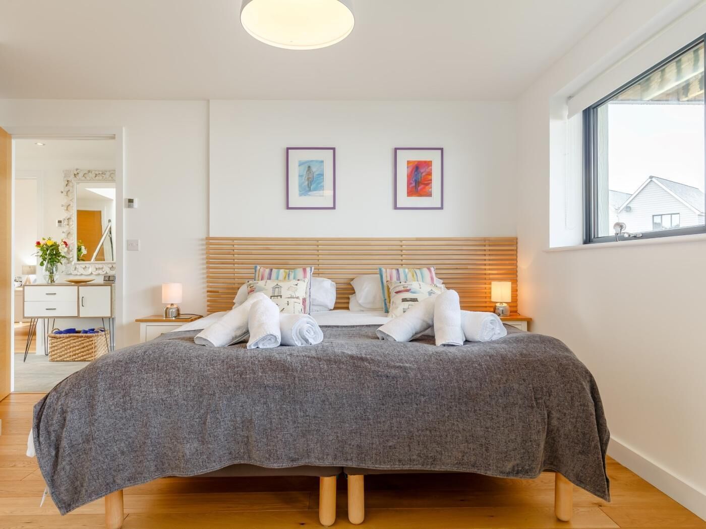 A neatly made bed with towels, a bedside table with a lamp, and two framed pictures on the wall.