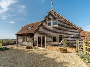 Ein Holzhaus mit geneigtem Dach, einem sichtbaren Schornstein und einer Zuwegung mit Kies.