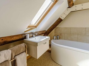 Ein Badezimmer mit Dachfenster, einer Badewanne, einem Waschbecken und einem Holzbalken.