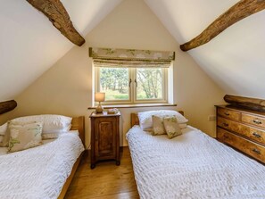 Ein Zimmer mit zwei Betten, einer Holzk dresser, einem Nachttisch mit Lampe und einem Fenster mit Blick auf Bäume.