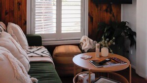A room with a bed, a round table with magazines, a TV, and a window with blinds.
