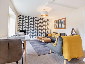 A modern living room with a sofa, a dining table, and a patterned wall. - 1 Bed in Aberaeron (oc-49261) (Aberaeron)