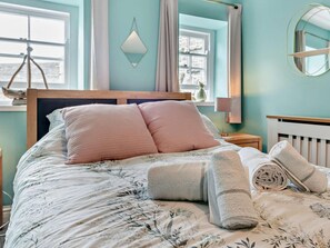 A bed with floral bedding, two pink pillows, a bedside lamp, and a rolled towel. - 1 Bed in Aberaeron (oc-49261) (Aberaeron)