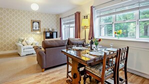 A dining area with a wooden table, chairs, a television, and a sofa. - 2 Bed in Cheltenham (oc-49336) (Woodmancote)