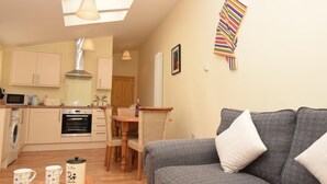 Een ruimtelijk ingerichte leefruimte met kitchenette, eethoek en een grijze bank met kussens.