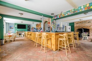 Un espace bar avec un comptoir et des tabourets en bois, une cheminée en briques et un mur décoré d’étiquettes de bières.