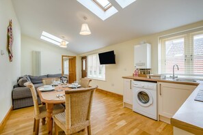 A compact living space with a dining area, sofa, washing machine, and a TV mounted on the wall. - 2 Bed in North Walsham (oc-49719) (Worstead)