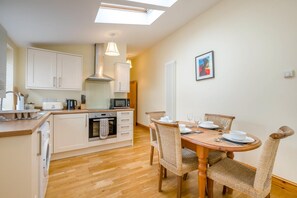 A compact kitchen with a dining area, including a microwave, oven, and a table set for two. - 2 Bed in North Walsham (oc-49719) (Worstead)