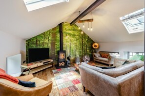 Ein Loft-Wohnzimmer mit großem Fernseher, Kamin und einer Wandmalerei von einem Wald.