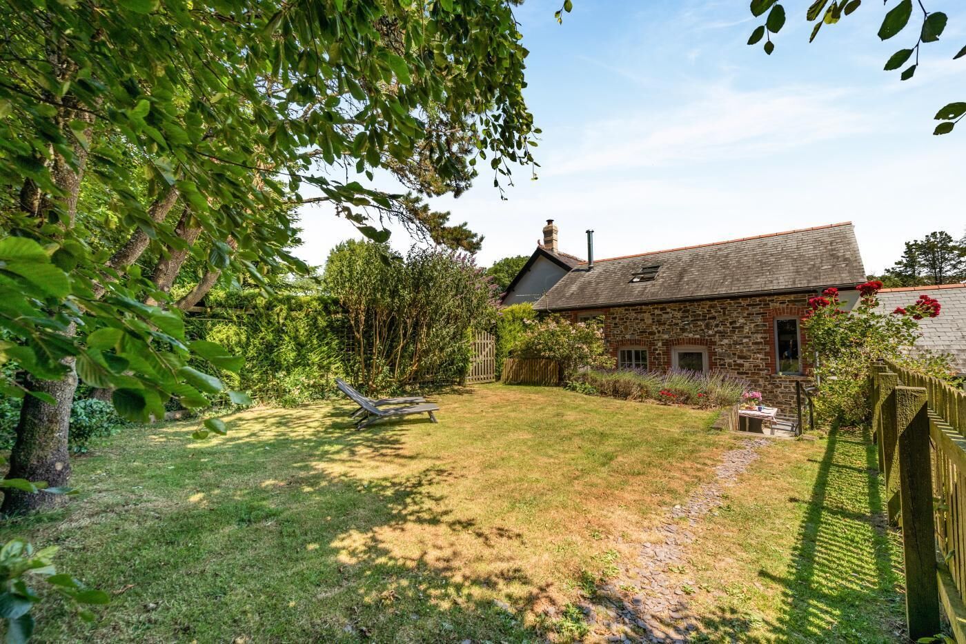 A stone house with a sloped roof, a lawn, and a wooden fence.