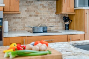 Une cuisine avec des meubles de rangement en bois, un mur recouvert de briques et un plan de travail sur lequel se trouvent une casserole et des légumes.