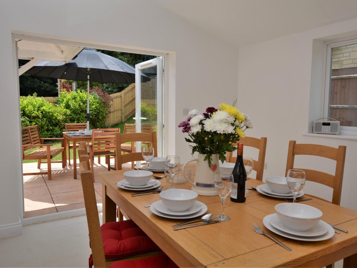 A dining area with a table set for four, a vase of flowers, and a radio on a windowsill.