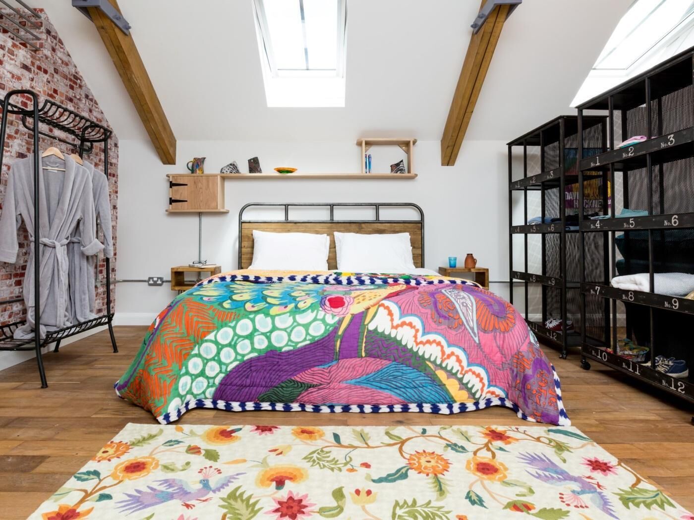 A bedroom with a bed, a wooden headboard, a window, a shelf with books, a rack with towels, and a storage unit with numbered compartments.
