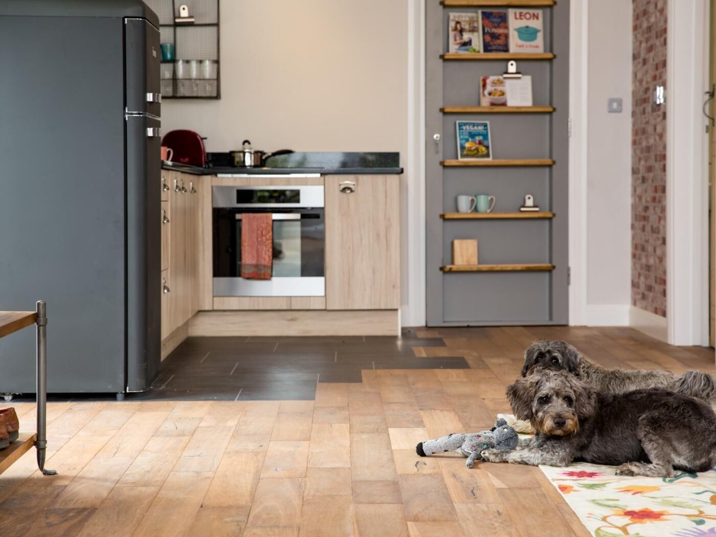 A kitchen with a refrigerator, oven, and wooden cabinets. There is a dog lying on the floor.