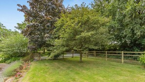 A fenced garden with a variety of trees and shrubs, a wooden gate, and a grassy area. - 1 Bed in Umberleigh (oc-49554) (High Bickington)