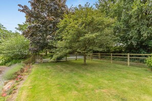 A fenced garden with a variety of trees and shrubs, a wooden gate, and a grassy area. - 1 Bed in Umberleigh (oc-49554) (High Bickington)