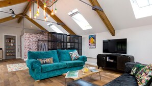 A spacious loft with exposed wooden beams, a teal sofa, a black leather couch, and a television. - 1 Bed in Umberleigh (oc-49554) (High Bickington)