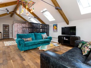 A spacious loft with exposed wooden beams, a teal sofa, a black leather couch, and a television. - 1 Bed in Umberleigh (oc-49554) (High Bickington)