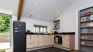 A modern kitchen with a black refrigerator, wooden cabinets, and a black countertop. - 1 Bed in Umberleigh (oc-49554) (High Bickington)