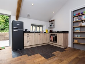 A modern kitchen with a black refrigerator, wooden cabinets, and a black countertop. - 1 Bed in Umberleigh (oc-49554) (High Bickington)