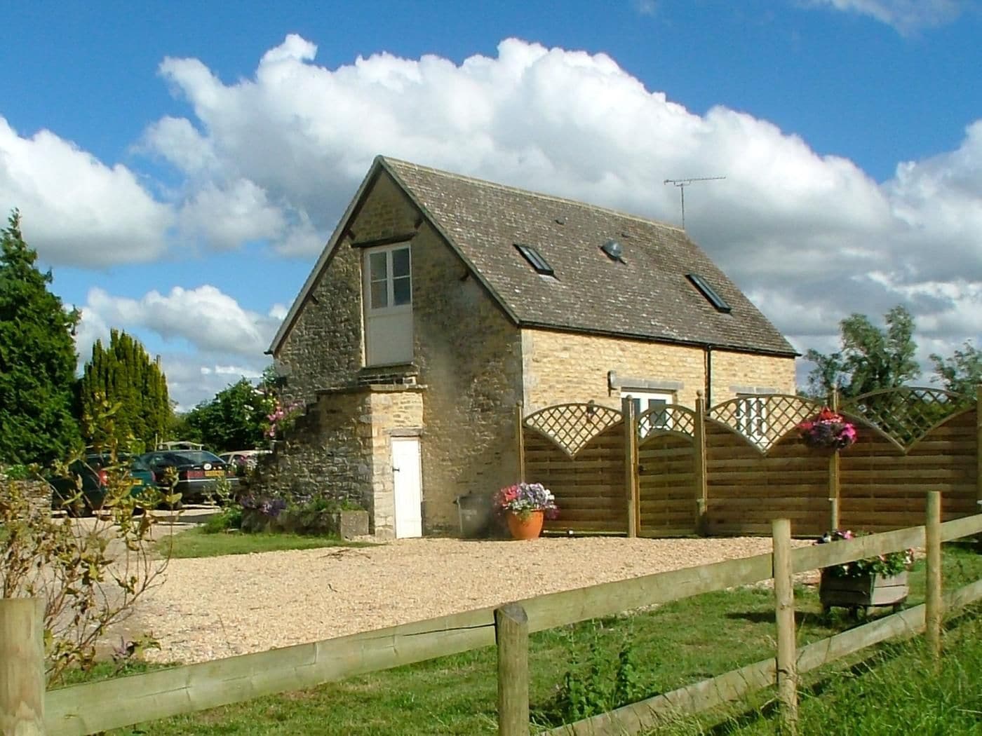 Une maison en pierre avec un toit en pente, une clôture en bois et une allée gravillonnée.