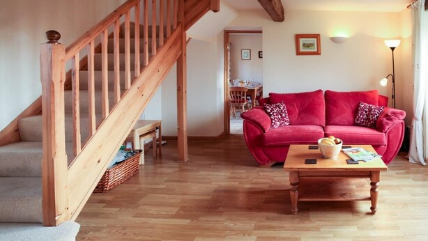 Eine Holztreppe, ein rotes Sofa, ein Holztisch und ein gemustertes Teppich in einem Wohnzimmer mit Holzboden.